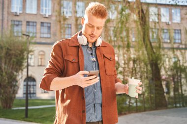 Kulaklık takan adam akıllı telefonundaki mesajları kontrol ediyor.