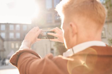 Güneş ışınlarında duran ve akıllı telefonunu tutan bir adam.