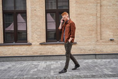 Şehir caddesinde yürüyen ve akıllı telefon kullanan biriyle sohbet eden adam.