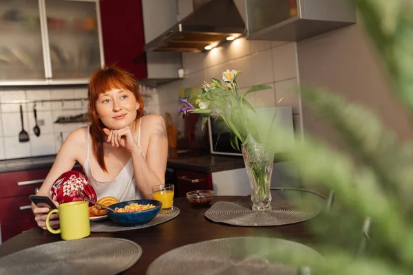 Woman having corn flakes with milk at the breakfast and looking at the window — Stock Photo, Image