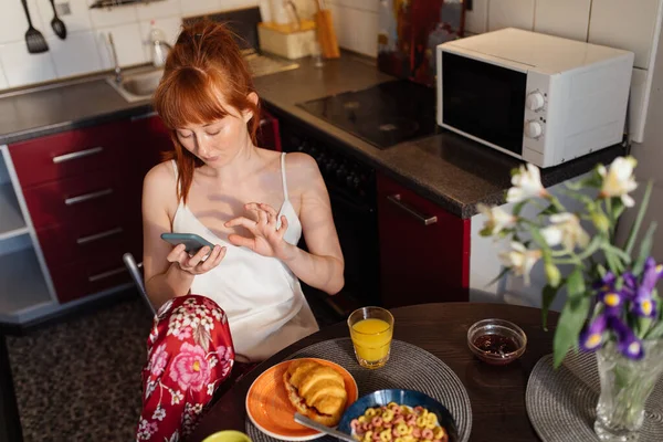 Mujer concentrada viendo algo en su smartphone mientras desayuna — Foto de Stock