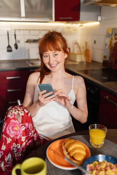 Ingwermädchen sitzt in der Küche und benutzt ihr Handy — Stockfoto