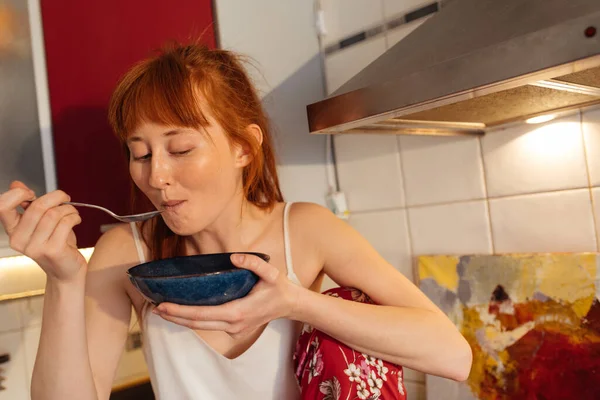 Woman with ginger hair eating corn flakes cereal while sitting and having breakfast — Stock Photo, Image