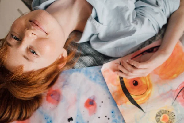 Ragazza in posa intorno alle sue immagini e sorridente mentre sdraiato sul letto — Foto Stock