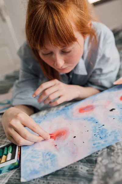 Zázvorová žena drží pastelky a pečlivě kreslí doma — Stock fotografie