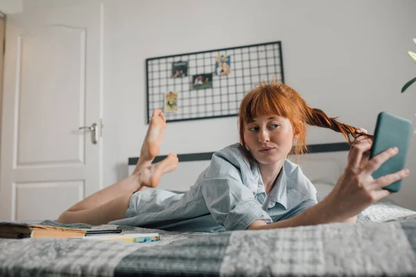 Mujer con pijama usando teléfono móvil en la cama, mientras se toma una selfie —  Fotos de Stock