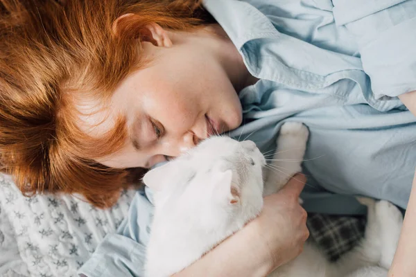 Žena objímající se se svou oblíbenou bílou kočkou při ležení na posteli — Stock fotografie