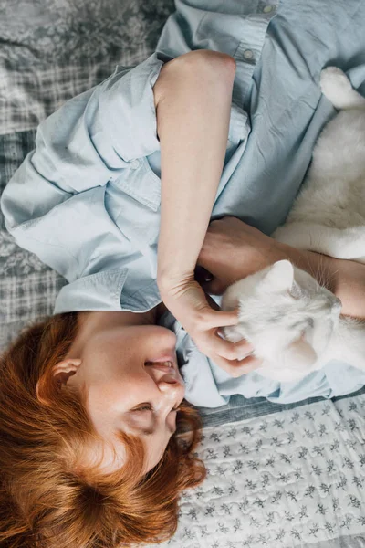 Mujer acostada en la cama y arañando a su gato blanco esponjoso — Foto de Stock