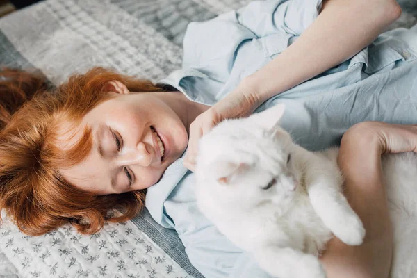 Žena objímající se se svou oblíbenou bílou kočkou při ležení na posteli — Stock fotografie