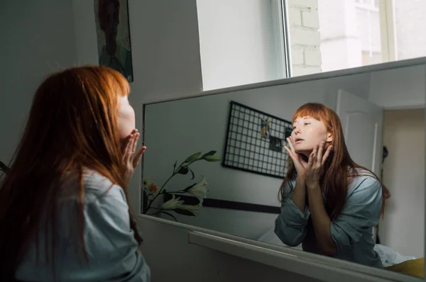 Mujer mirándose al espejo, tocándose la cara y sintiéndose satisfecha — Foto de Stock