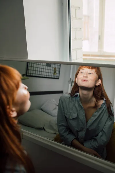 Ginger woman with under eyes patches admiring herself while looking at the mirror — Stock Photo, Image