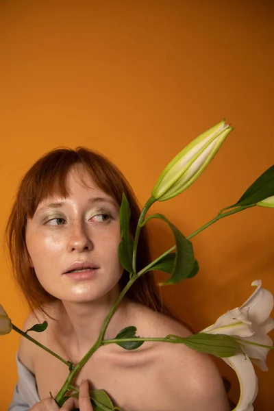 Roodharige vrouw kijken weg terwijl poseren met lelies in de studio — Stockfoto