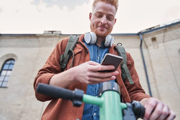 Mannen som står på den motordrivna scootern och låser upp den via smartphone — Stockfoto