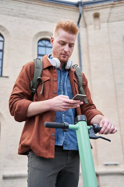 Man som håller mobiltelefon och låser upp med det powered scooter — Stockfoto