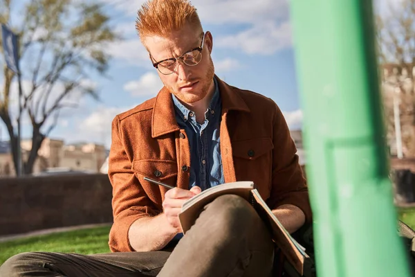 Чоловік в окулярах пише в блокнот, проводячи час на природі — стокове фото