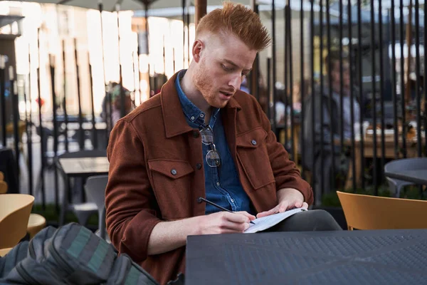 Hombre sentado en el café y tomando notas mientras trabaja — Foto de Stock