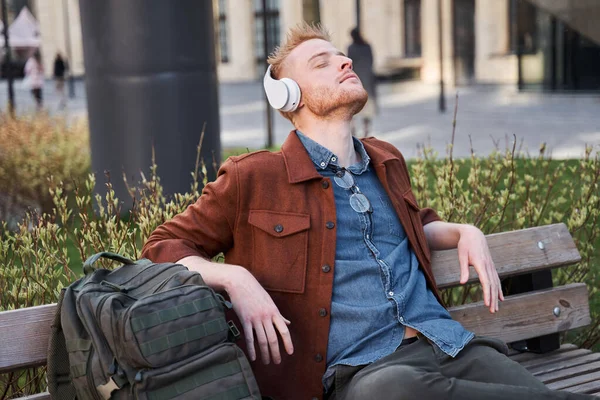 나무 의자에서 헤드폰을 풀고 눈을 감고 앉아 있는 사람 — 스톡 사진