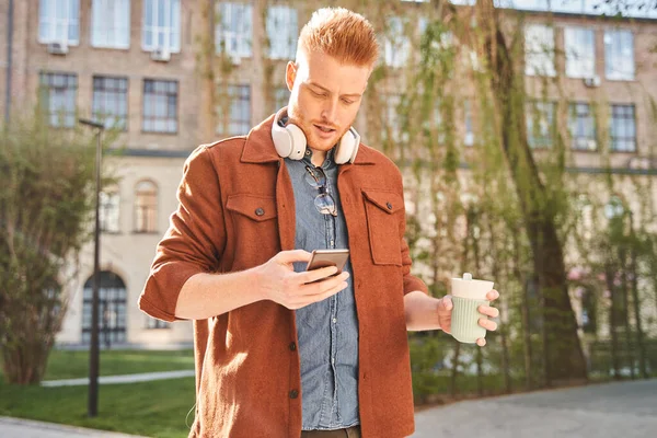 Kulaklık takan adam akıllı telefonundaki mesajları kontrol ediyor.