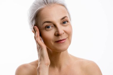 Mükemmel yumuşak yüzlü bir kadın kameraya bakıyor ve poz verirken gülümsüyor.