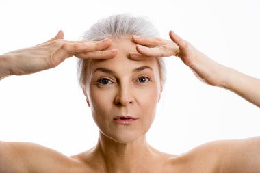 Kadın elleriyle alnına dokunuyor ve küçük kırışıklıklarını gösteriyor.