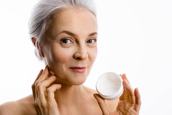 Старшая женщина надевает крем для лица и увлажняет кожу