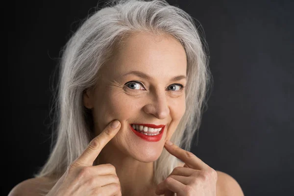Oude vrouw raakt haar huid op het gezicht en glimlachende tand aan de camera — Stockfoto