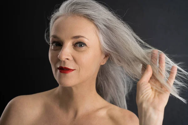 Mulher de pé isolado no fundo preto e tocando seu cabelo — Fotografia de Stock