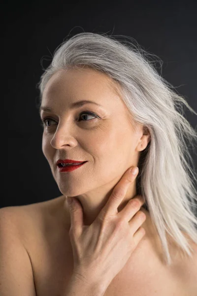 Aging woman touching her neck and smiling warmly — Stock Photo, Image