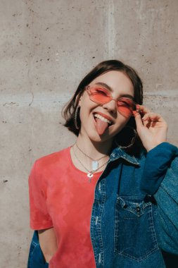 Pembe güneş gözlüğü takan kadın kameraya bakıyor ve dilini gösteriyor.