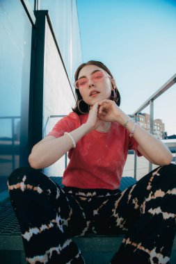 Sokak tarzı güneş gözlüğü takan kız merdivenlerde oturuyor.