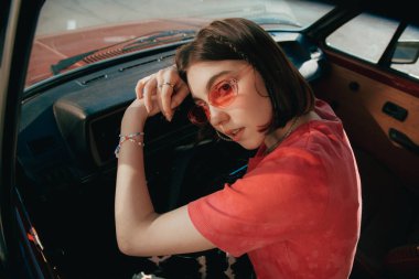 Kız kameraya bakıyor ve arabada otururken direksiyonda yatıyor.