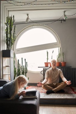 Lotus pozisyonunda oturan ve evde zaman geçirirken meditasyon yapan bir adam.