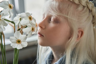 Masada duran ve vazodaki çiçekleri koklayan kız.