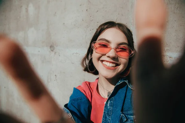 Girl wearing pink sunglasses smiling widely and stretching her hands to the camera — Stock Photo, Image