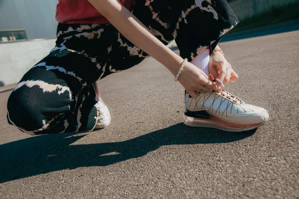 Дівчина сидить на вулиці і зав'язує кросівки під час прогулянки в літньому місті — стокове фото