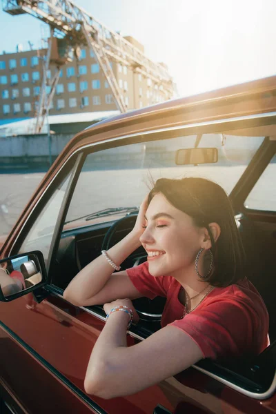 Усміхнена дівчина сидить у машині і дивиться на вікно під час охолодження — стокове фото
