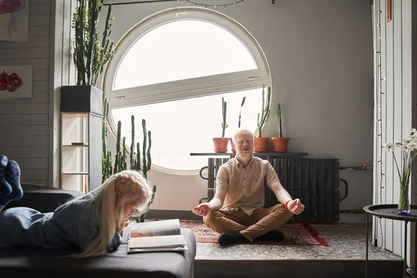 Hombre practicando yoga y sentado en posición de loto en el suelo con los ojos cerrados —  Fotos de Stock