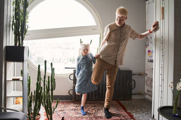 Albino child doing morning exercises with her blonde father at home