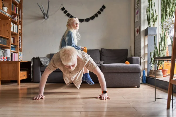 Een man in huishoudkleding die push-ups doet met zijn dochter op zijn rug. — Stockfoto