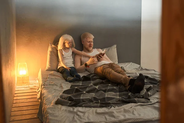 Menina mostrando algo no livro para seu pai enquanto sentado na cama — Fotografia de Stock