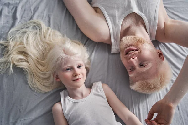 Meisje liggend op de grijze deken met haar albino vader terwijl het doorbrengen van tijd thuis — Stockfoto