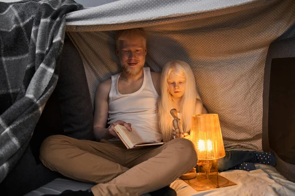 Man zit aan de chalabuda met zijn kleine blonde dochter en leesboek — Stockfoto