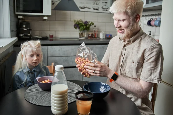 Ojciec siedzi przy stole ze swoją blond córką i przygotowuje płatki kukurydziane — Zdjęcie stockowe