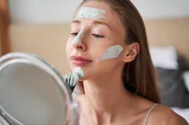 Vitiligo hastalığı olan bir kadın aynanın önünde oturmuş kollarında tutuyor.