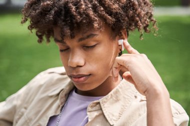 Kablosuz kulaklık takan adam yürürken temiz havada gözleri kapalı dinleniyor.