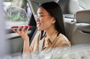 Arabanın arka koltuğunda oturan bir kadın birine sesli mesaj kaydediyor.