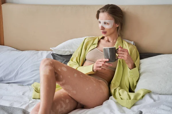 Mulher aplicando máscara facial deitada na cama e olhando para a janela — Fotografia de Stock