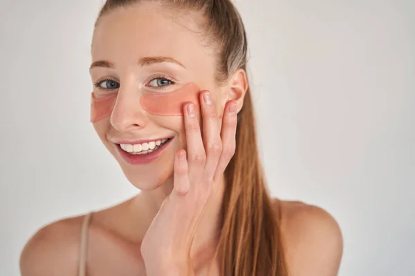 Woman wearing under eye patches touching her skin with satisfaction