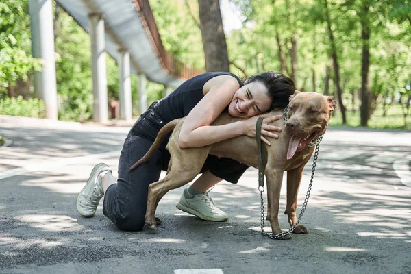 Женщина обнимает свою смешную коричневую собаку, сидя на дороге — стоковое фото