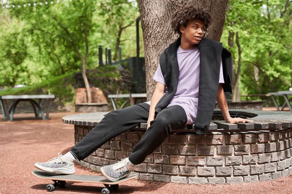 Skateboarder seduto alla panchina e guardando altrove mentre si gode — Foto Stock